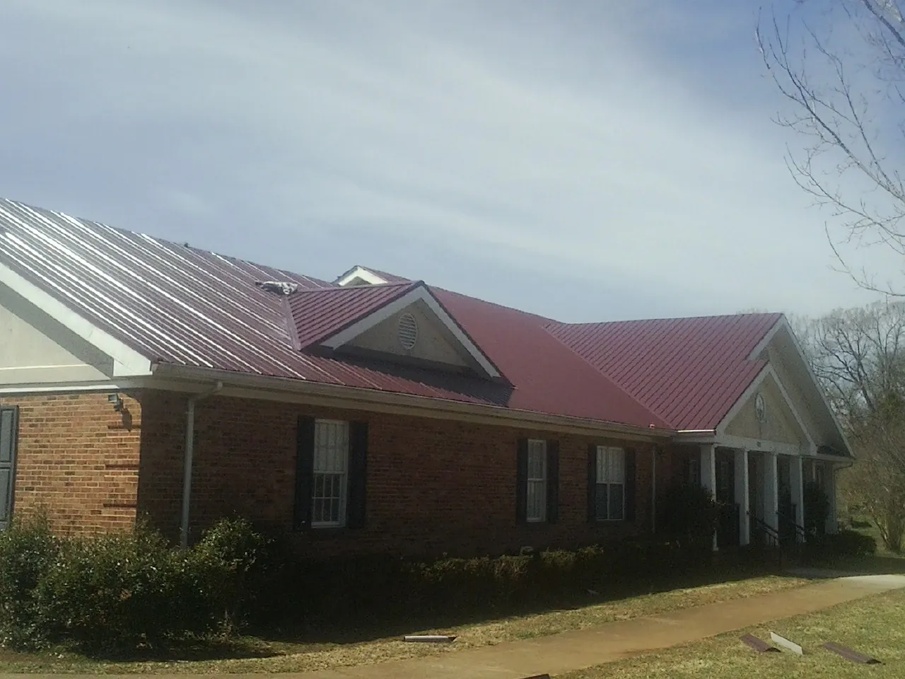 Red metal roof with gabled entries on a long brick building, from a Hail Damage Roof Repair job in Newton Lower Falls