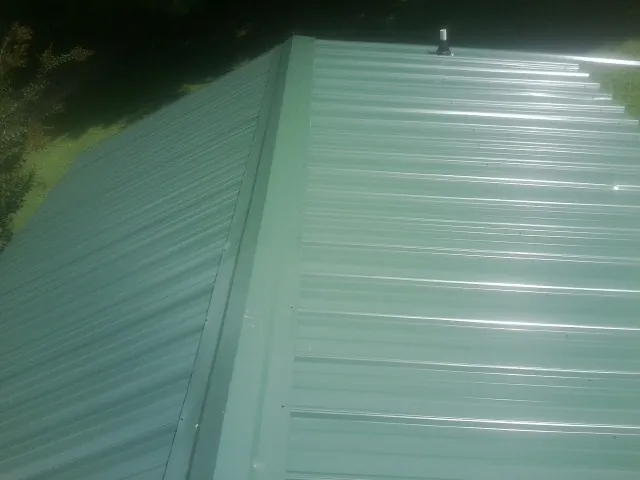 New green metal panels meeting at the ridge of a roof — Flat Roof Repair work by our crew in Newton Lower Falls