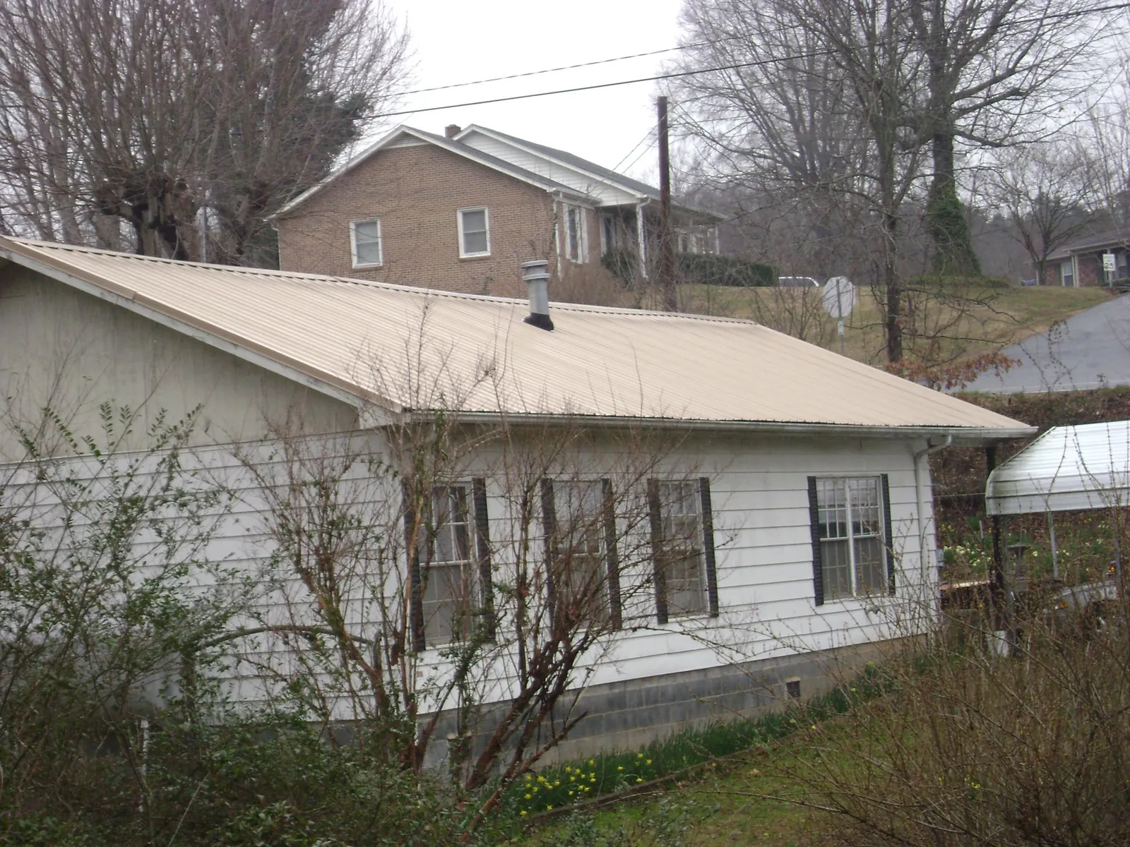 Tan metal roof on a white sided house set into a hillside — Commercial Roofing by Roofing Brothers in Newton Lower Falls